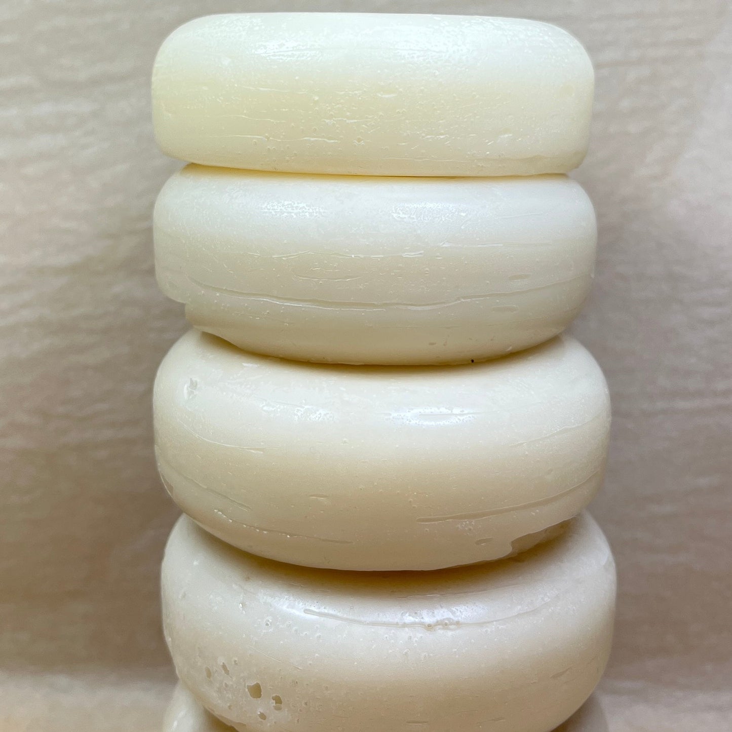 A stack of four round hair conditioner bars with a smooth texture, in a natural off-white color.