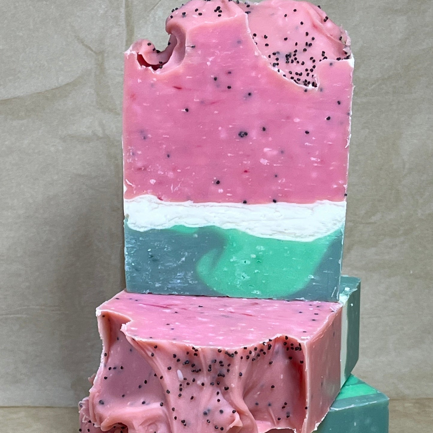 A stack of handmade soap bars with layered pink and green colors, and black speckles throughout.