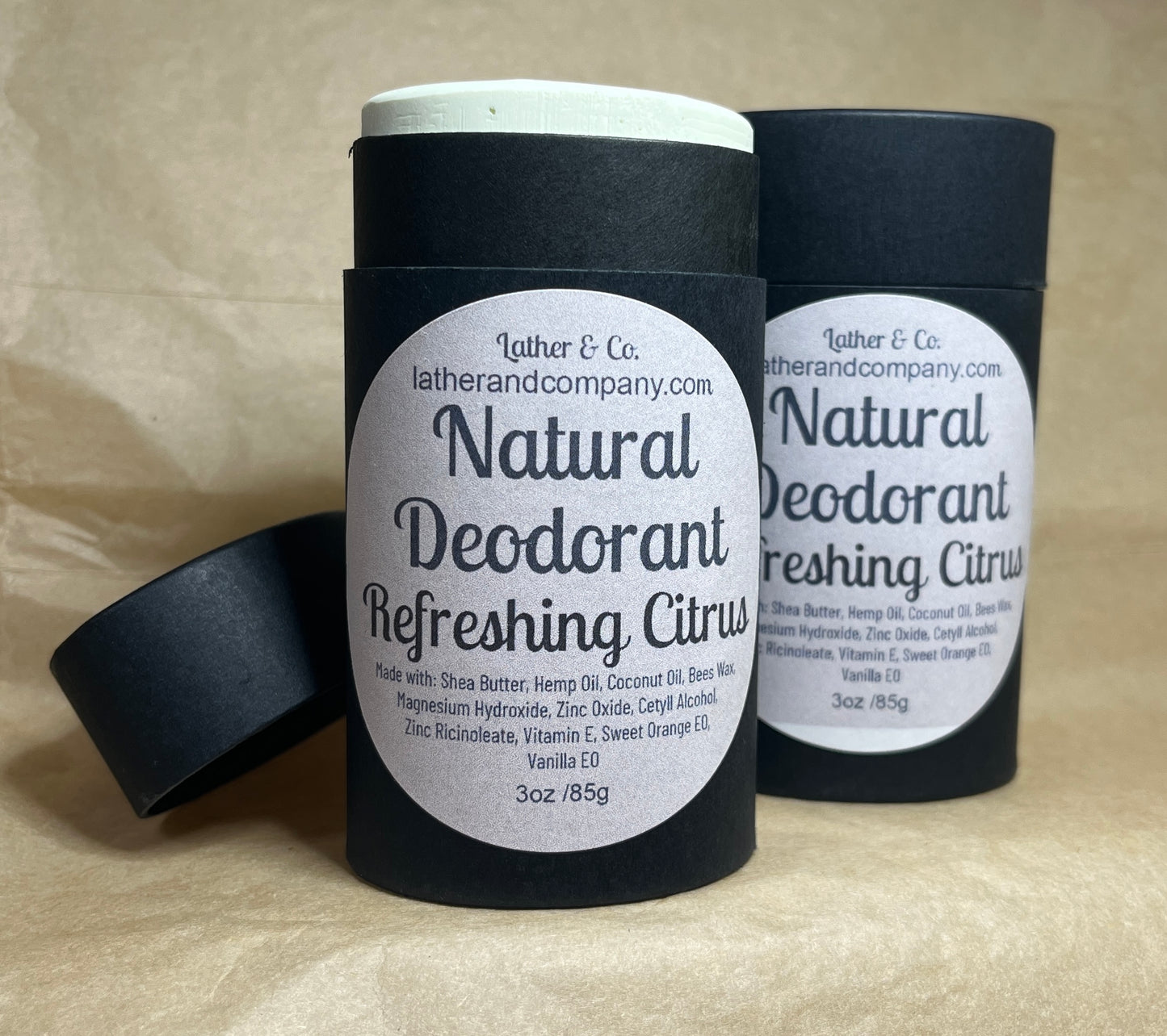 Two cylindrical eco-friendly paperboard deodorant tubes with black lids. The labels indicate the scent is either Lavender Tea Tree or Refreshing Citrus, and the brand is Lather & Co.