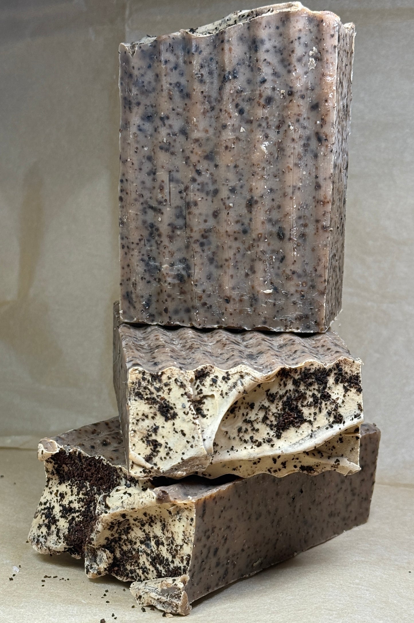 Stack of dark-colored soap bars with speckles on a neutral background