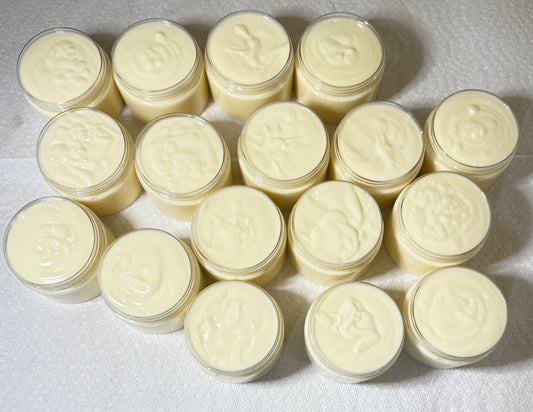 Multiple small jars of body butter arranged in a grid pattern on a light-colored surface.